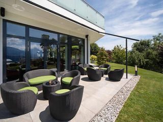 Modern hotel patio with chic black rattan furniture and vibrant green cushions, overlooking a scenic mountain view